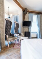 Quarto com cama, duas poltronas estofadas, televisão e teto decorativo.