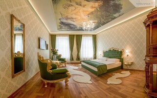 Um quarto luxuoso com uma cama grande, mobiliário dourado e verde ornamentado, um candelabro e um mural no teto.