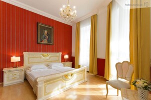 Quarto de hotel com uma cama grande, duas mesas de cabeceira, um candelabro e uma cadeira.