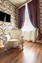 Quarto com poltrona clássica, papel de parede estampado e uma grande janela com cortinas.