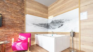 Uma casa de banho moderna com uma banheira branca, chão de madeira, uma cadeira rosa e um espelho fixado na parede.