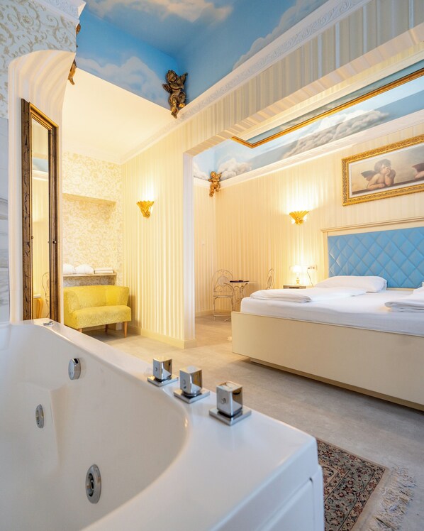 A luxurious bedroom with a large bed, a separate sitting area, and a bathtub.