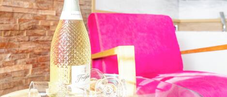 A room with a wooden wall, a glass table with a bottle and glasses, and a pink chair.