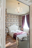 Quarto com cabeceira estofada, candelabro, papel de parede estampado e um espelho grande.