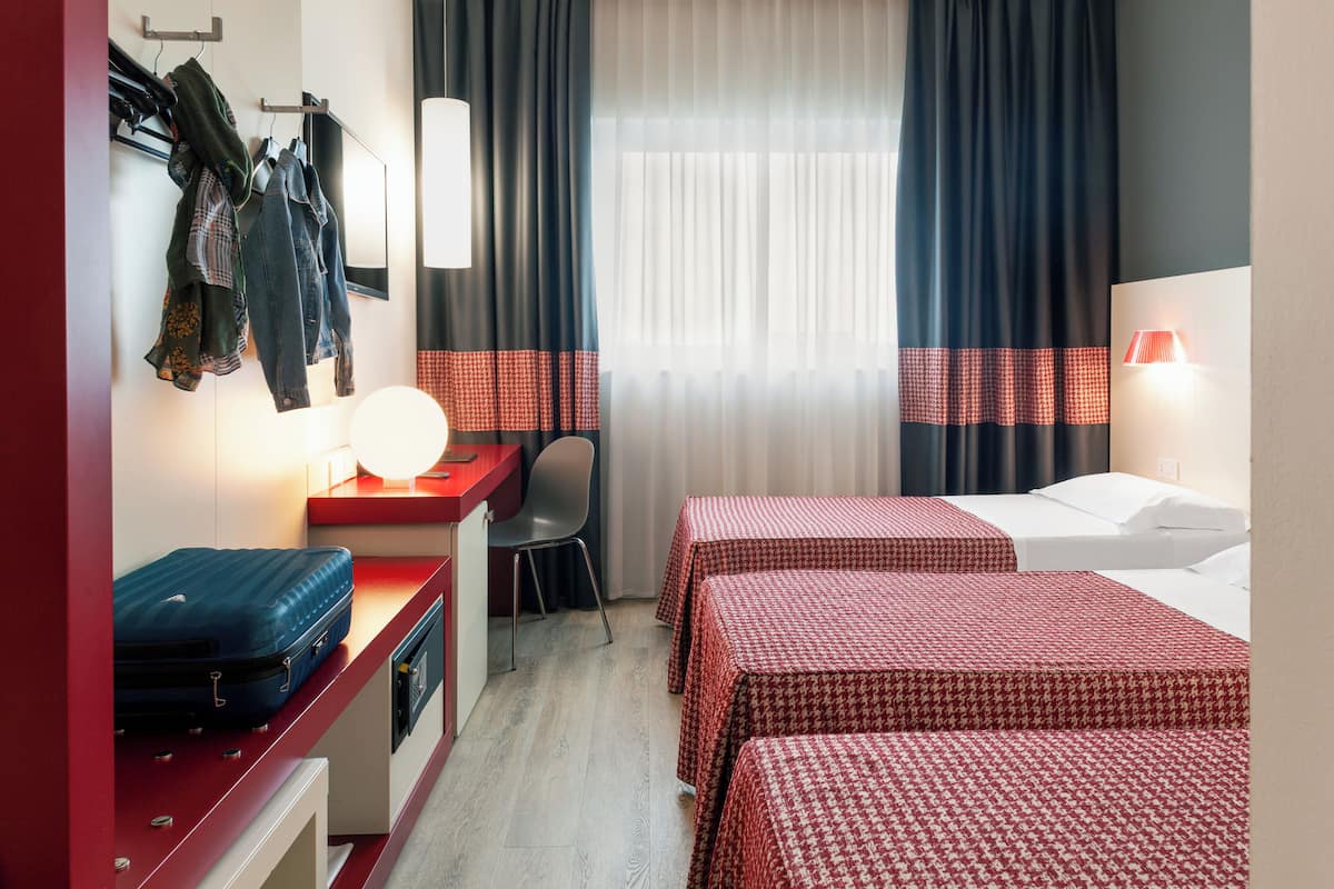 A hotel room with two beds, a desk with a suitcase, a chair, and a coat rack.