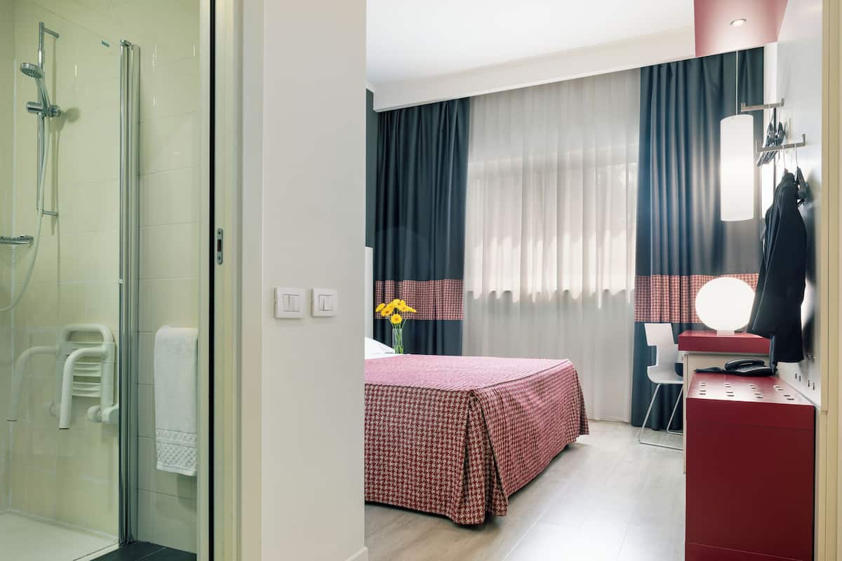 A hotel room with a shower, bed, desk, and a mirror.