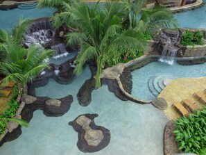 A pool area with multiple waterfalls, palm trees, and a seating area with lounge chairs. - The Springs Resort and Spa at Arenal (Monterrey)