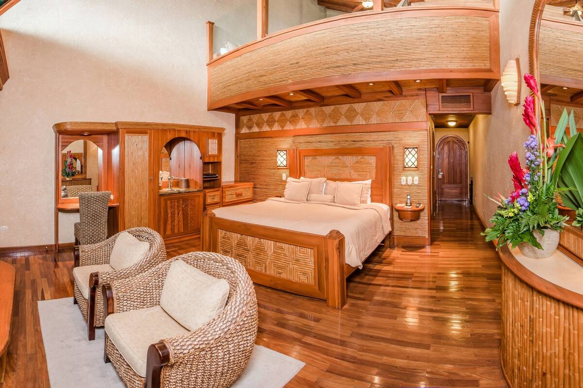 A spacious bedroom with a large bed, wooden furniture, and a curved wooden ceiling.