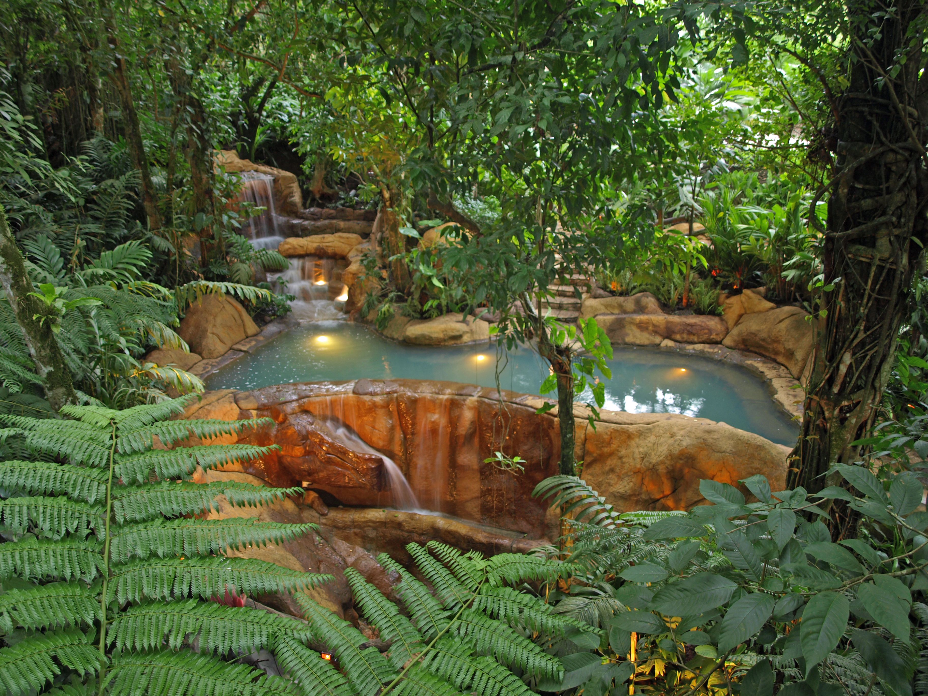Ein üppiger Innenbereich mit einem Garten und einem zentralen Wasserspiel, einschließlich eines Wasserfalls und eines Teichs.