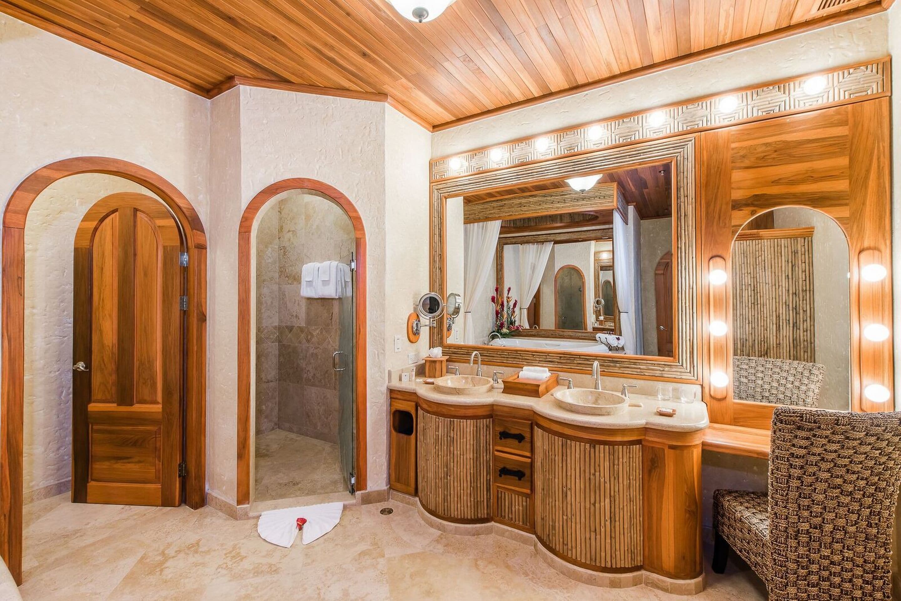 A luxurious bathroom with wooden vanity, multiple sinks, a large mirror, and a shower area.
