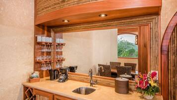 Una cocina con un espejo grande, estantes de madera con utensilios de cocina, un lavabo y una ventana con vista a la vegetación.