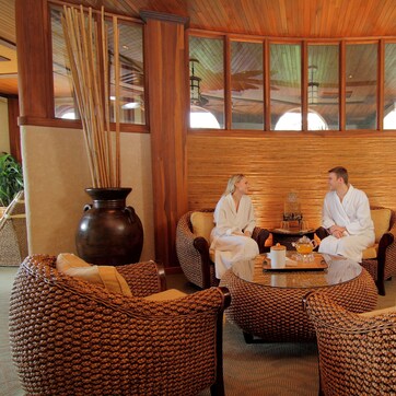 A room with a round glass table, wicker furniture, and large vases.