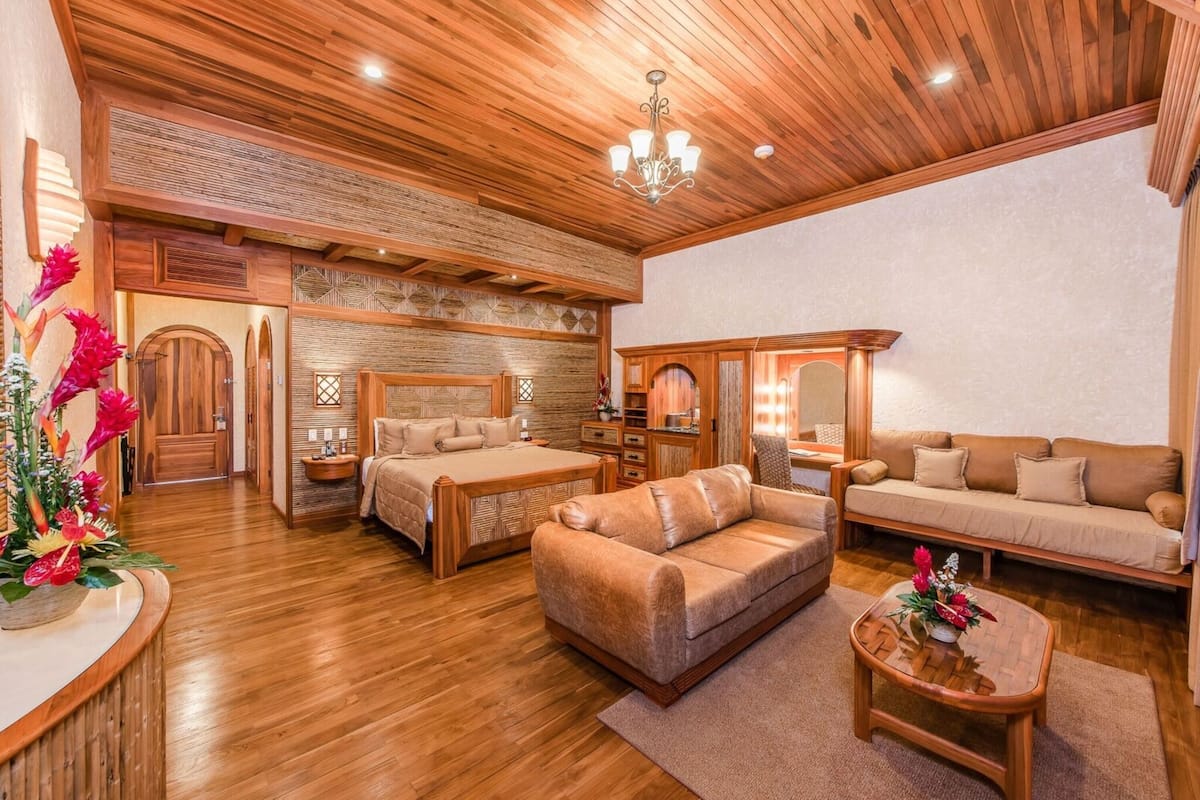 A spacious room with a wooden ceiling, a large bed, a sofa, and a small table.