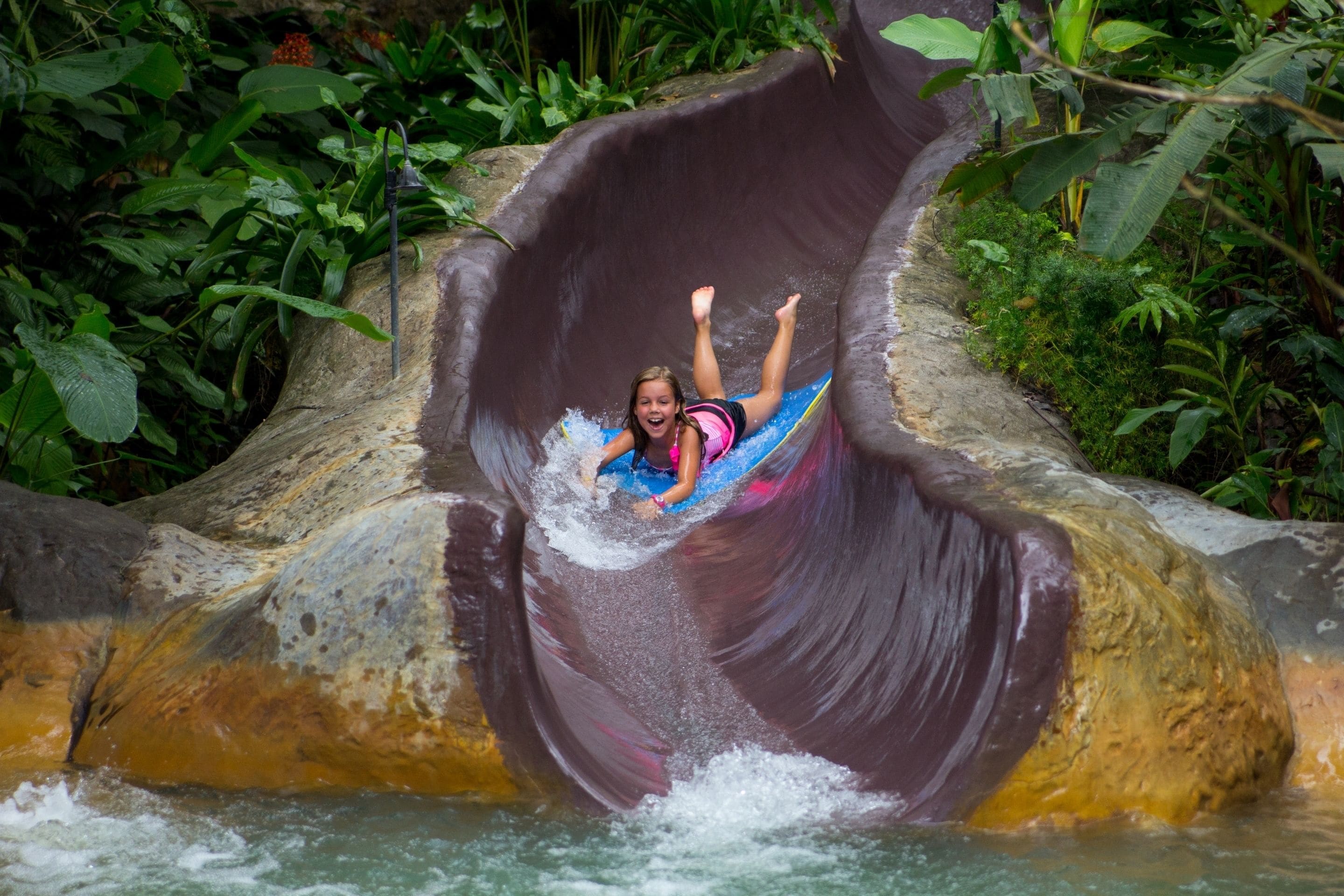 A person sliding down a water slide surrounded by lush greenery.
