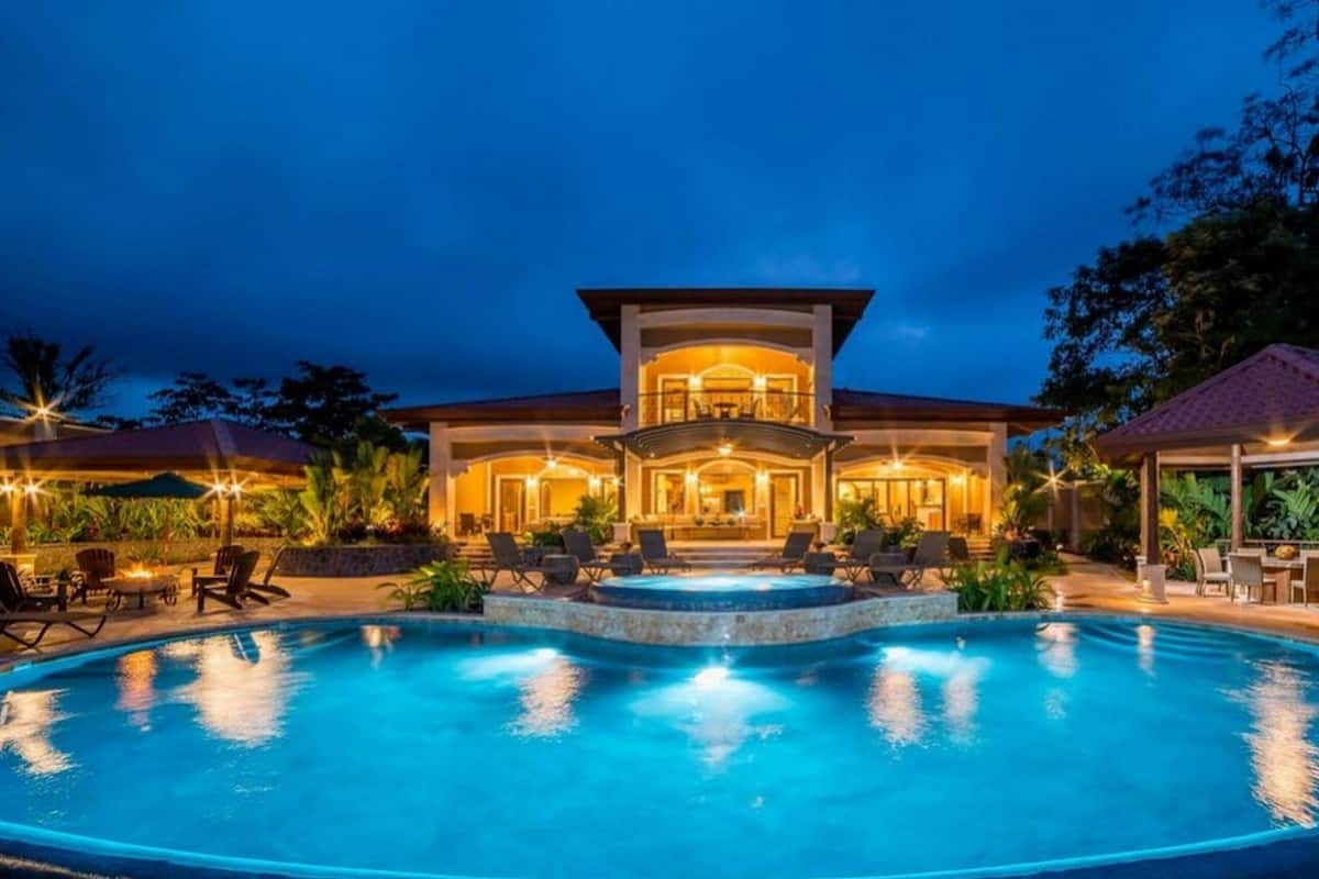 A large, well-lit house with a swimming pool in the foreground.