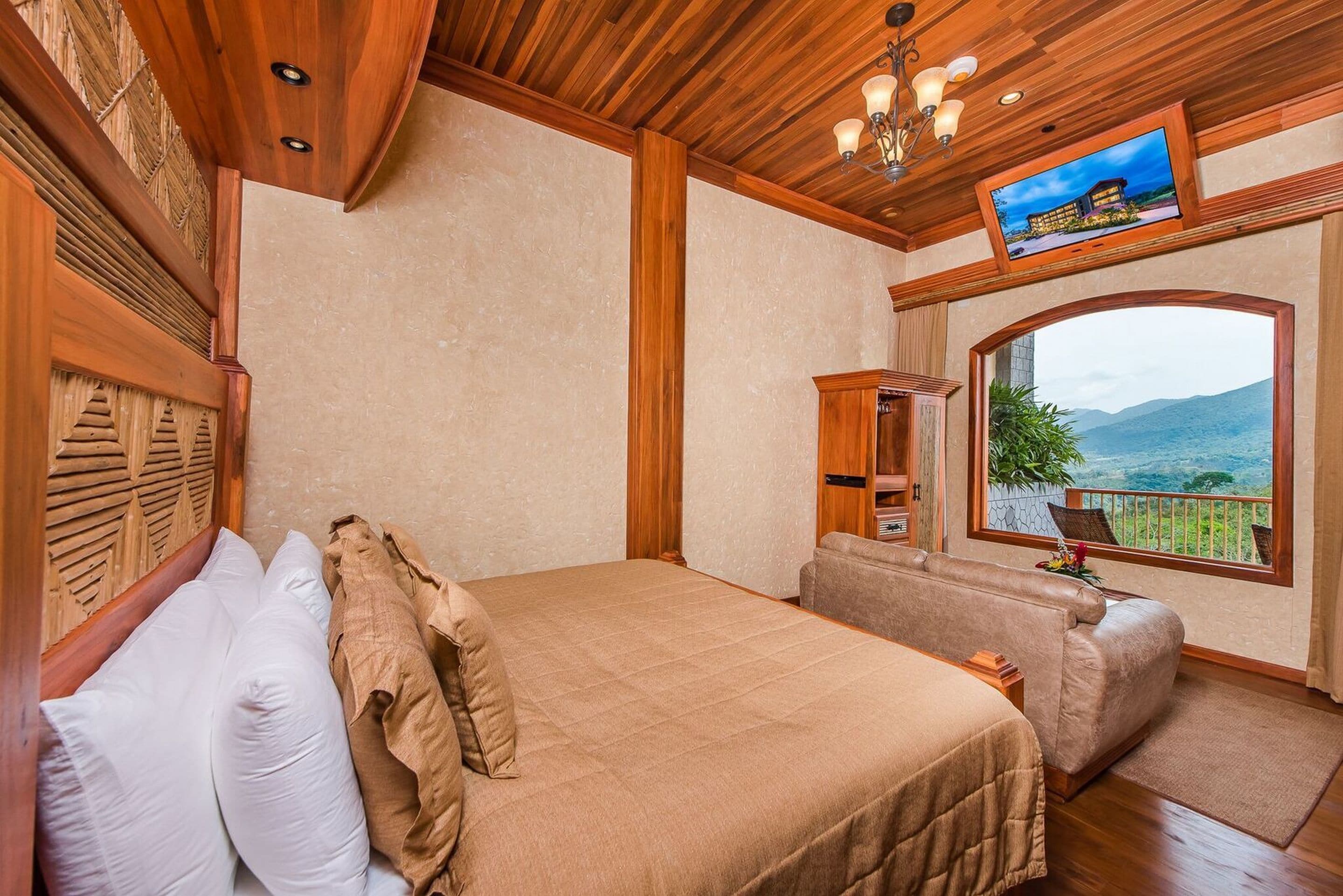 Un dormitorio con cama, televisor, ventana con vistas y techo de madera.