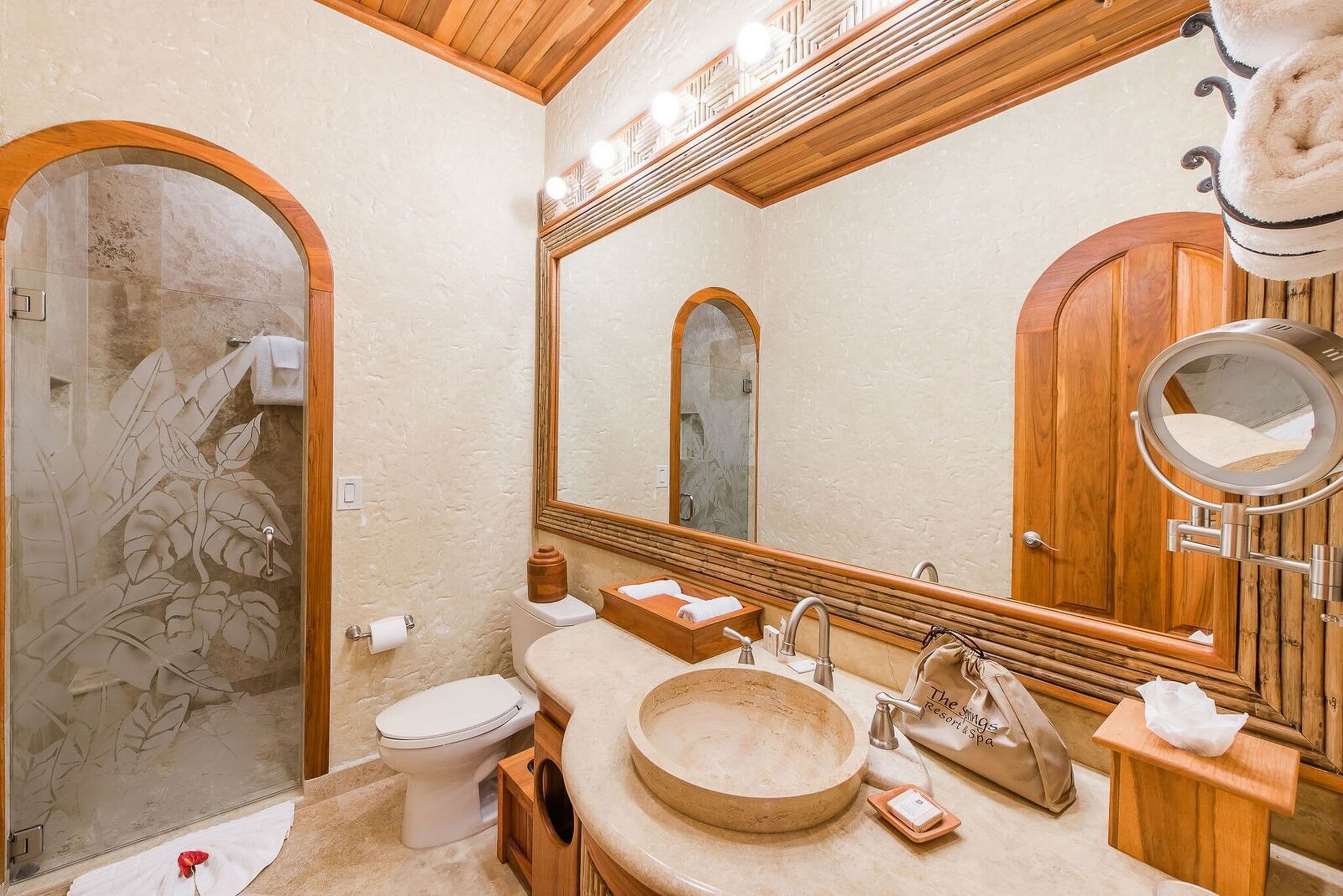 A bathroom with a wooden vanity, a large mirror, a round sink, and a glass shower enclosure.