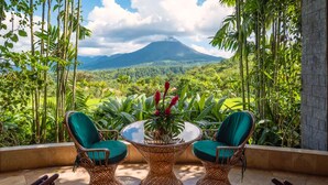 Un patio con sillas de mimbre y una mesa de vidrio, con vista a un paisaje exuberante y una montaña.