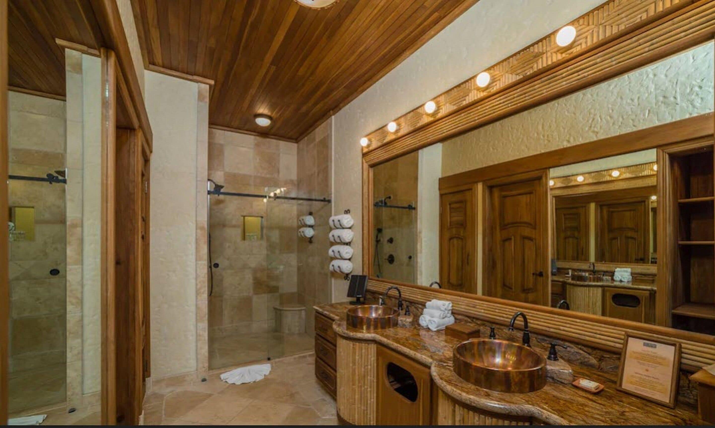 A bathroom with a large mirror, wooden vanity, and a shower area.