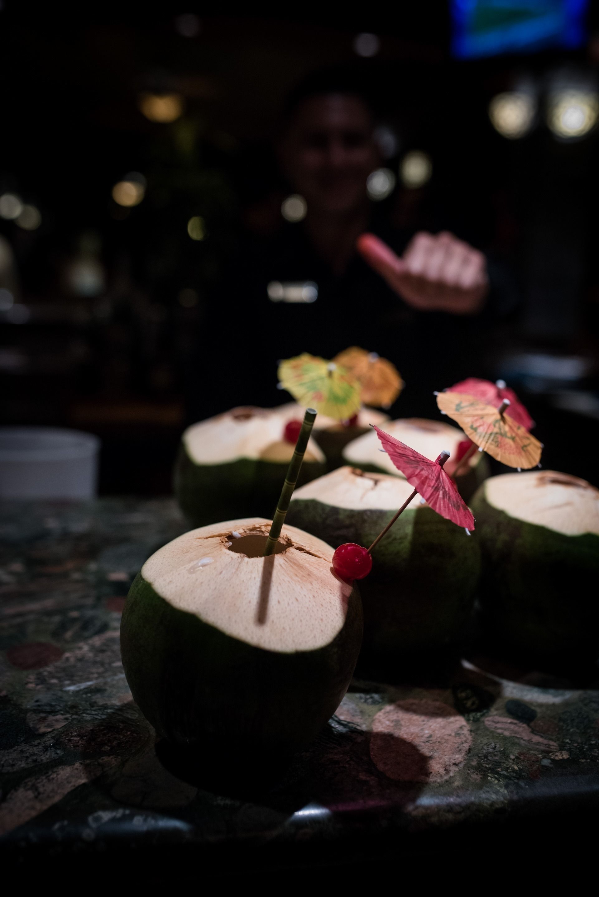 A bar counter with several coconut drinks garnished with umbrellas and cherries.