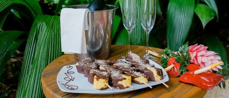 Una mesa de madera con un plato de dulces bañados en chocolate, una botella de champán y dos copas.