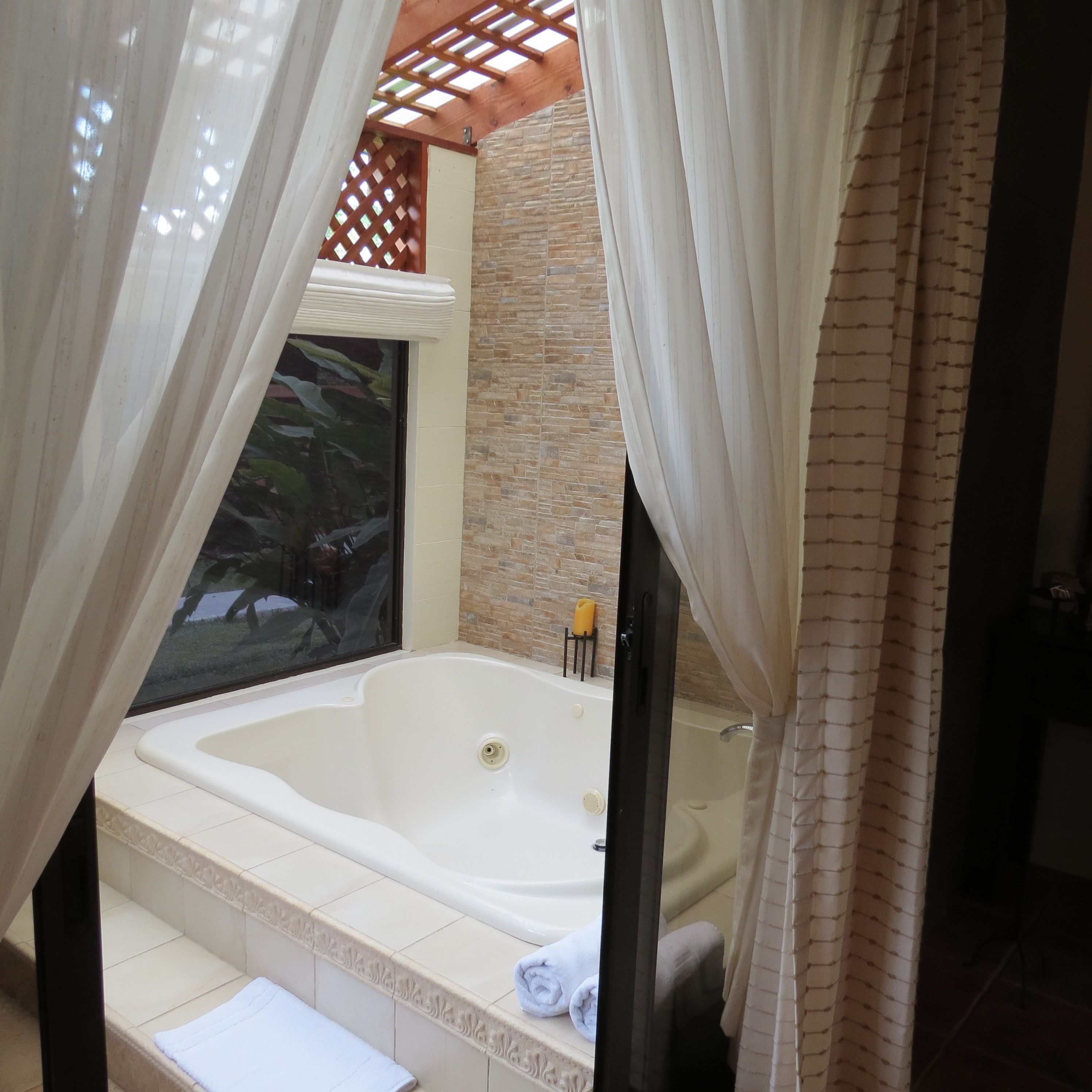 A bathroom with a large bathtub, a shower, and a window with a view of greenery.