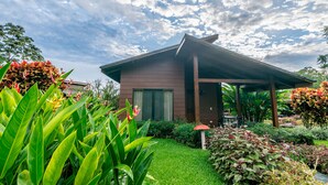 A modern house with a covered porch, surrounded by lush greenery and flowering plants.
