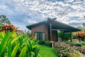 A modern house with a covered porch, surrounded by lush greenery and flowering plants.