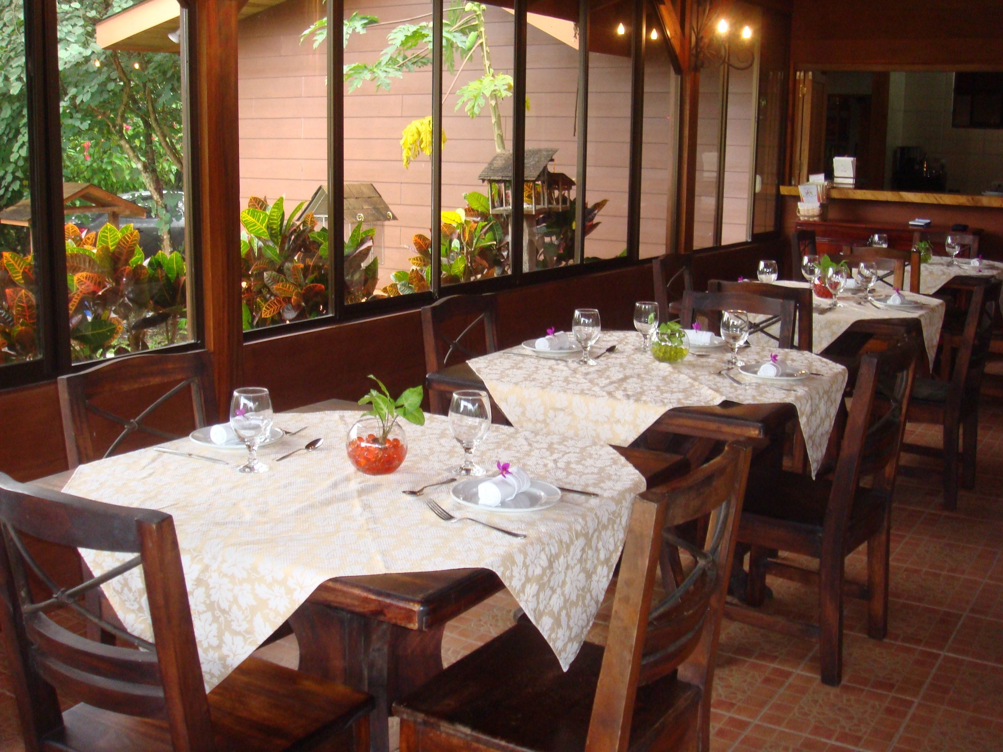 A restaurant with multiple tables set for dining, featuring a view of greenery outside.