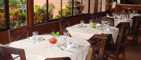 A restaurant with multiple tables set for dining, featuring a view of greenery outside.