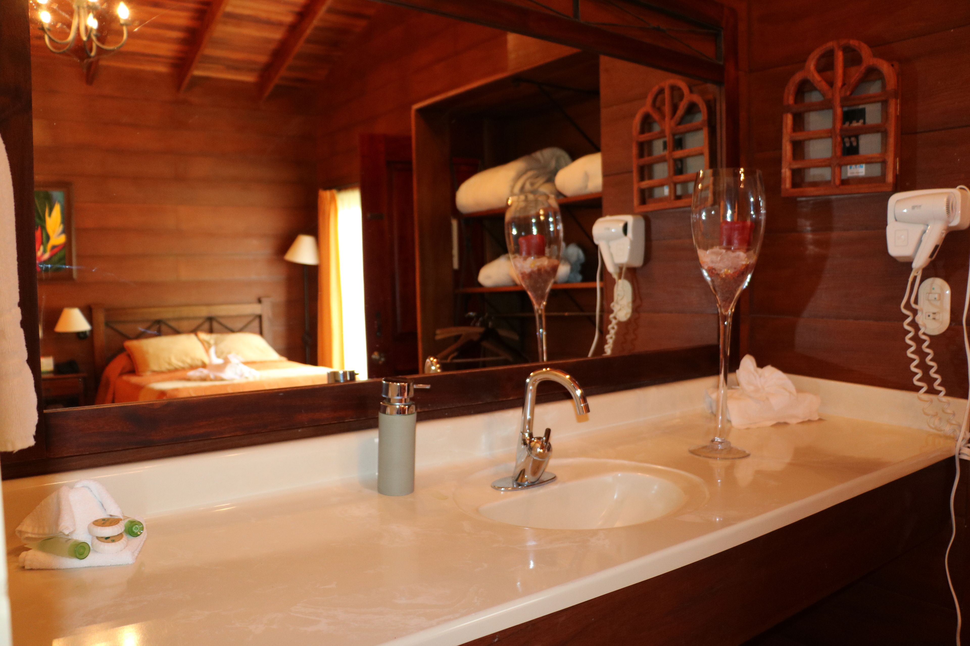 Un baño con detalles de madera, un espejo grande, un lavamanos y dos copas de vino.
