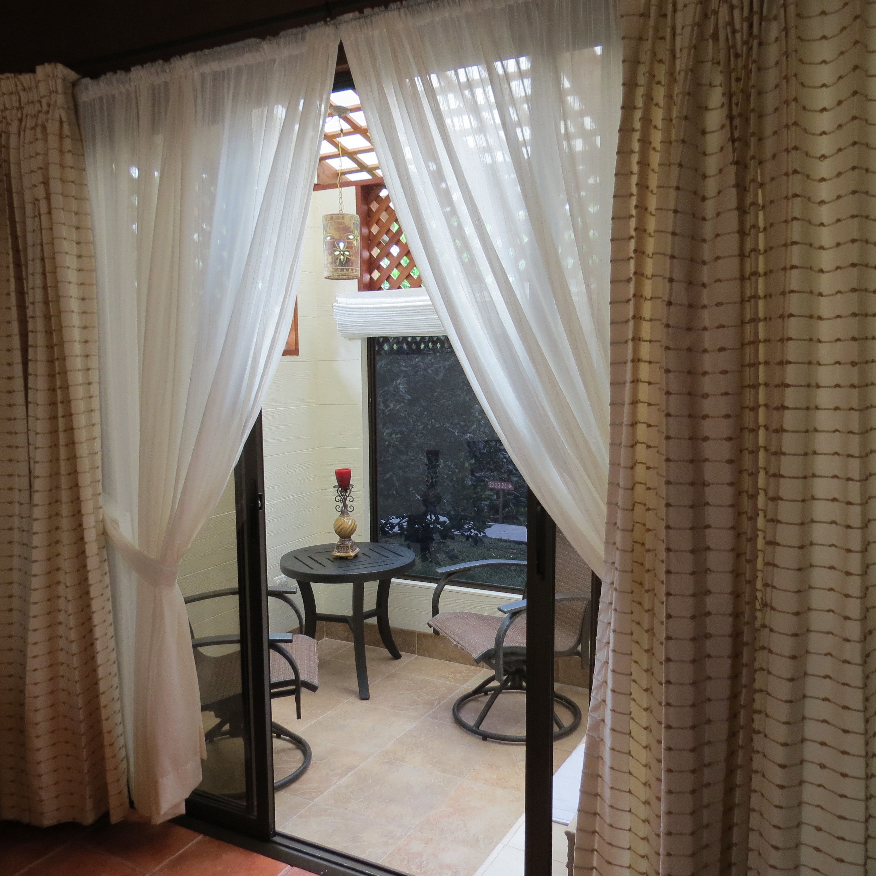 A room with a glass door, white curtains, a small round table with a candle, and two chairs.