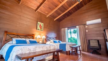 A room with two beds, a wooden ceiling, a window with curtains, and a desk with a chair.