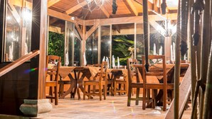A wooden interior with tables and chairs, a chandelier, and large windows.