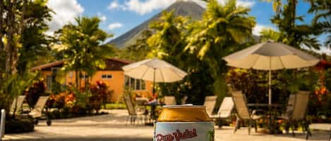 A can of 'Pure Vida!' beer on a poolside with a view of a mountain and palm trees.