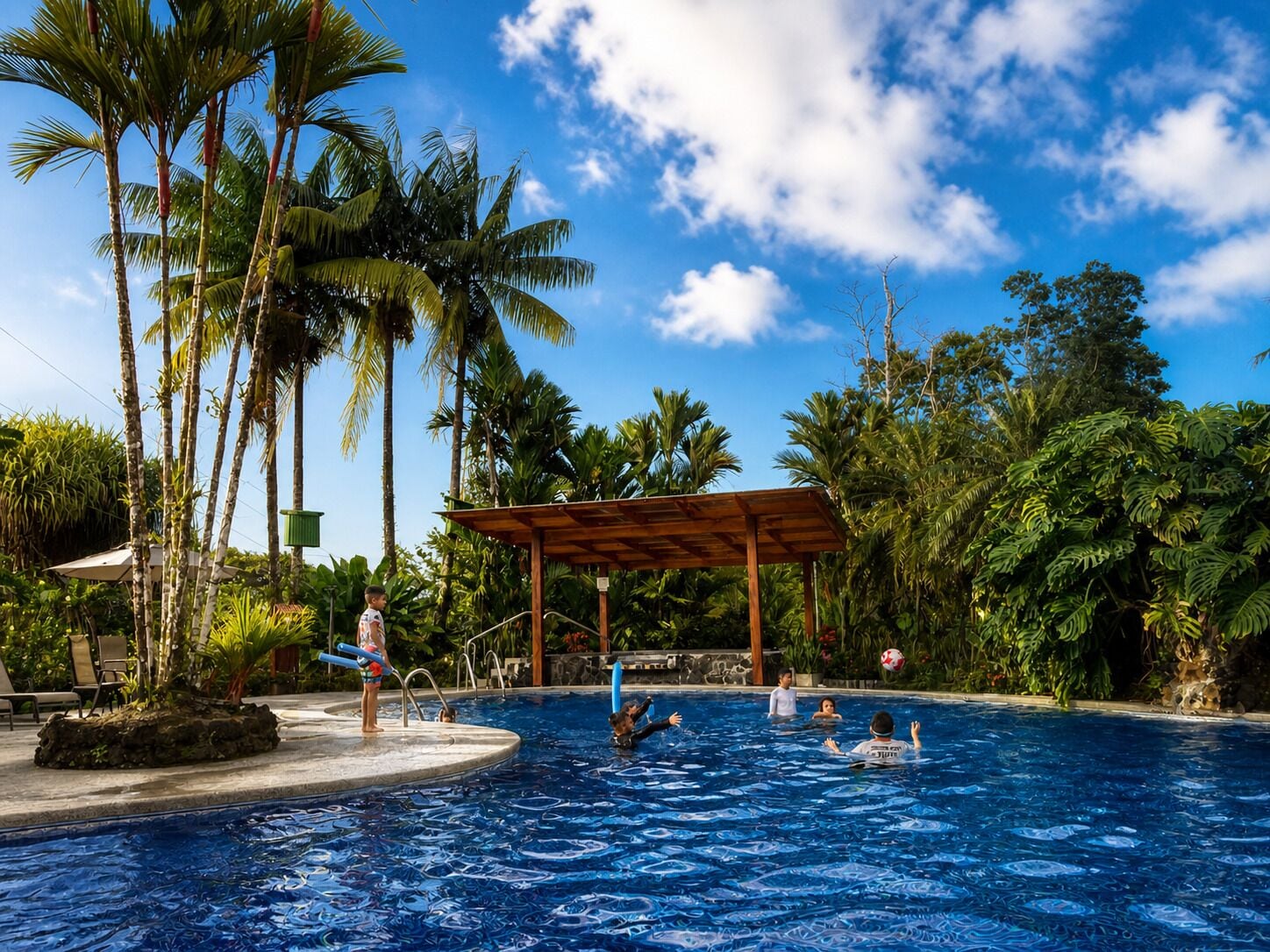 A swimming pool with palm trees and a covered area.