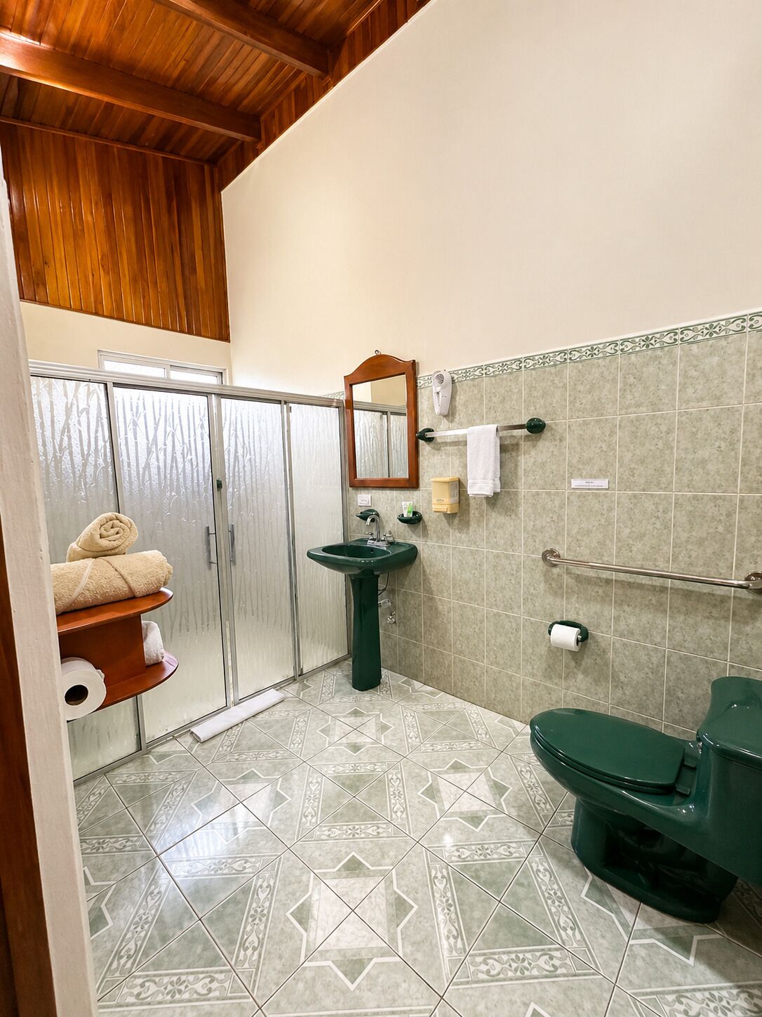 A bathroom with a green sink, a toilet, a shower with a glass door, and a towel rack with towels.
