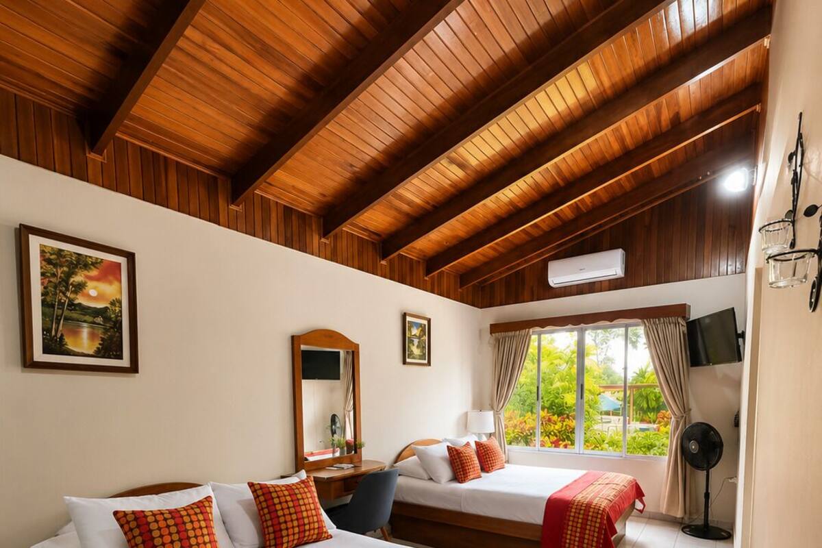 Camera d'albergo con due letti, travi in legno a soffitto, un'ampia finestra e una televisione a schermo piatto.