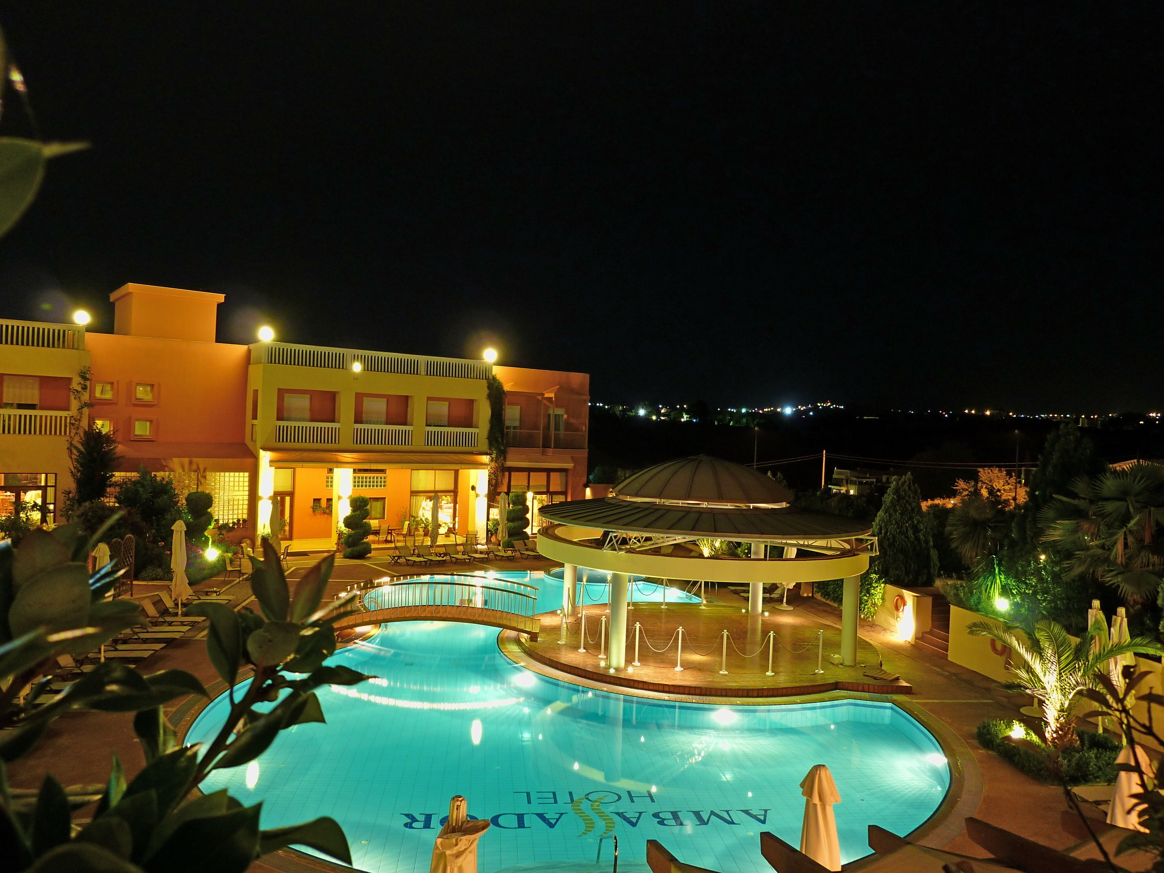 A swimming pool with a gazebo, surrounded by palm trees and a hotel building with multiple floors and balconies.