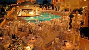 Un espace de restauration aménagé au bord de la piscine, avec des tables rondes dressées pour les clients, entourées de parasols et de chaises.