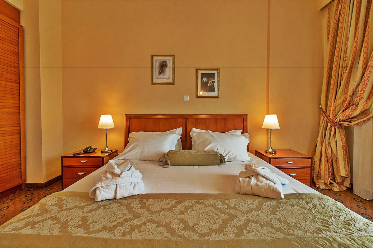 A hotel room with a large bed, two bedside tables, a headboard, and two wall-mounted lamps.