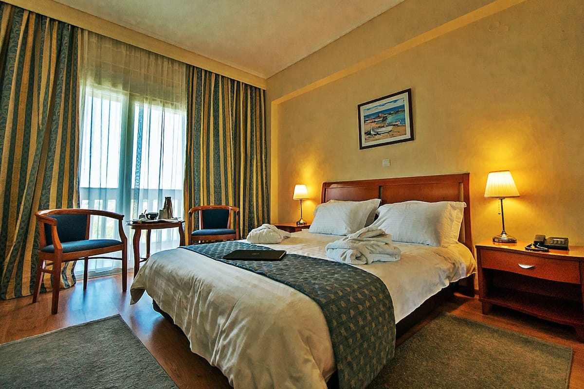 A hotel room with a large bed, two bedside tables with lamps, a chair, and a painting on the wall.