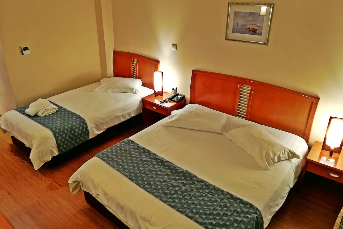 A hotel room with two beds, wooden headboards, bedside tables with lamps, and a framed picture on the wall.