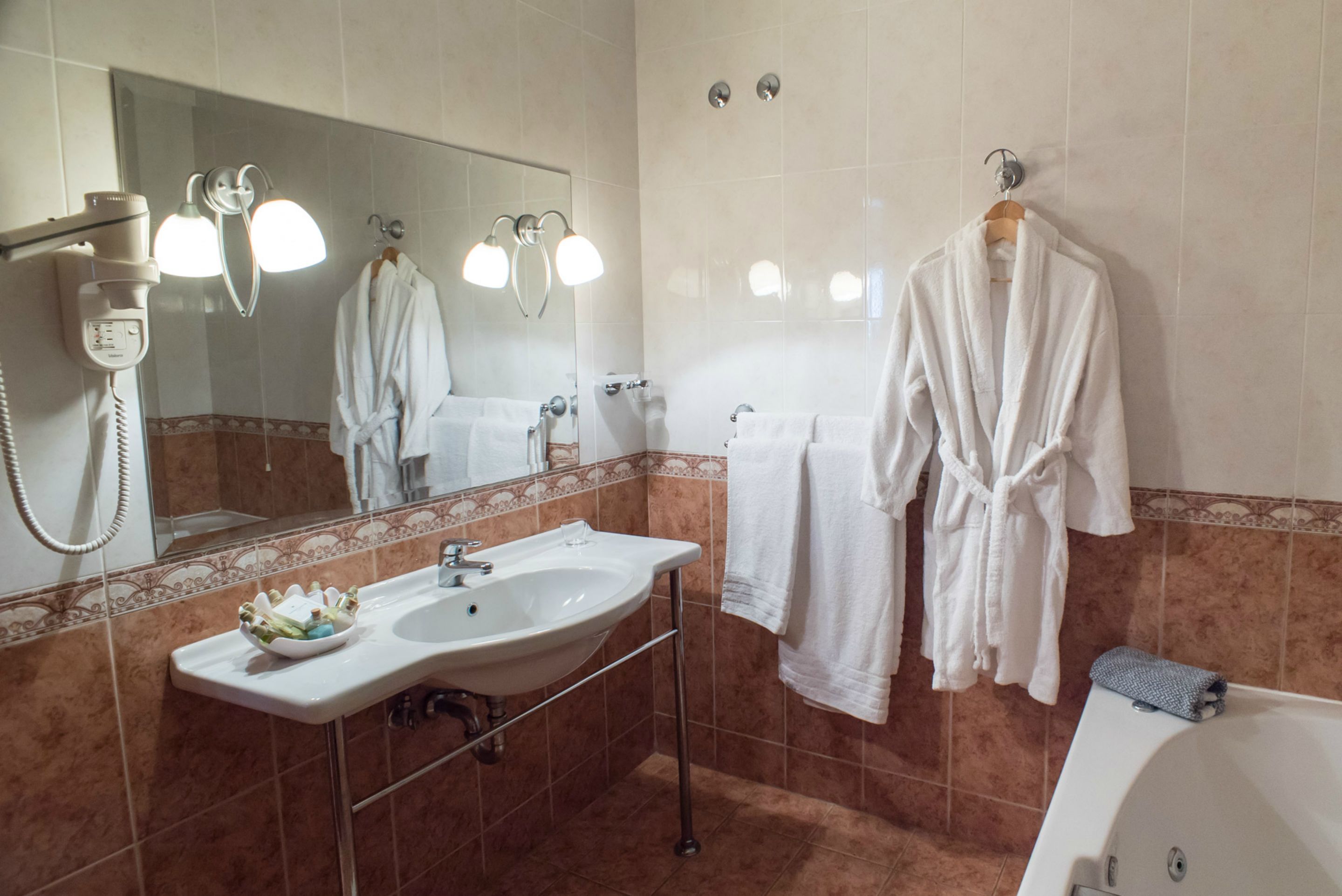 A bathroom with a sink, mirror, robe hooks, and a towel rack.