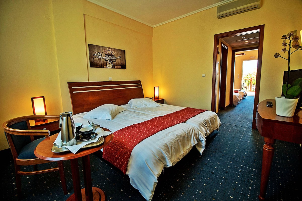 A hotel room with a bed, bedside table, chair, and a painting on the wall.