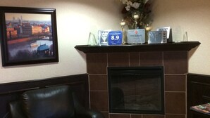 A lobby with a fireplace, a framed cityscape painting, a black leather chair, and a reception desk with a price sign. - Comfort Inn & Suites Edson - Yellowhead Highway (Edson)