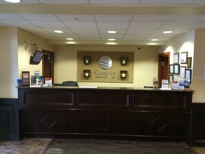 A reception desk with a sign for Comfort Inn & Suites, a bulletin board, and framed certificates on the wall.