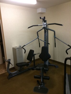 A gym with various exercise equipment including a multi-directional machine, a bench, and a small weight machine.