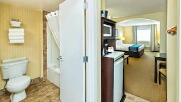 A hotel bathroom with a toilet, shower, and a sink area with a microwave.