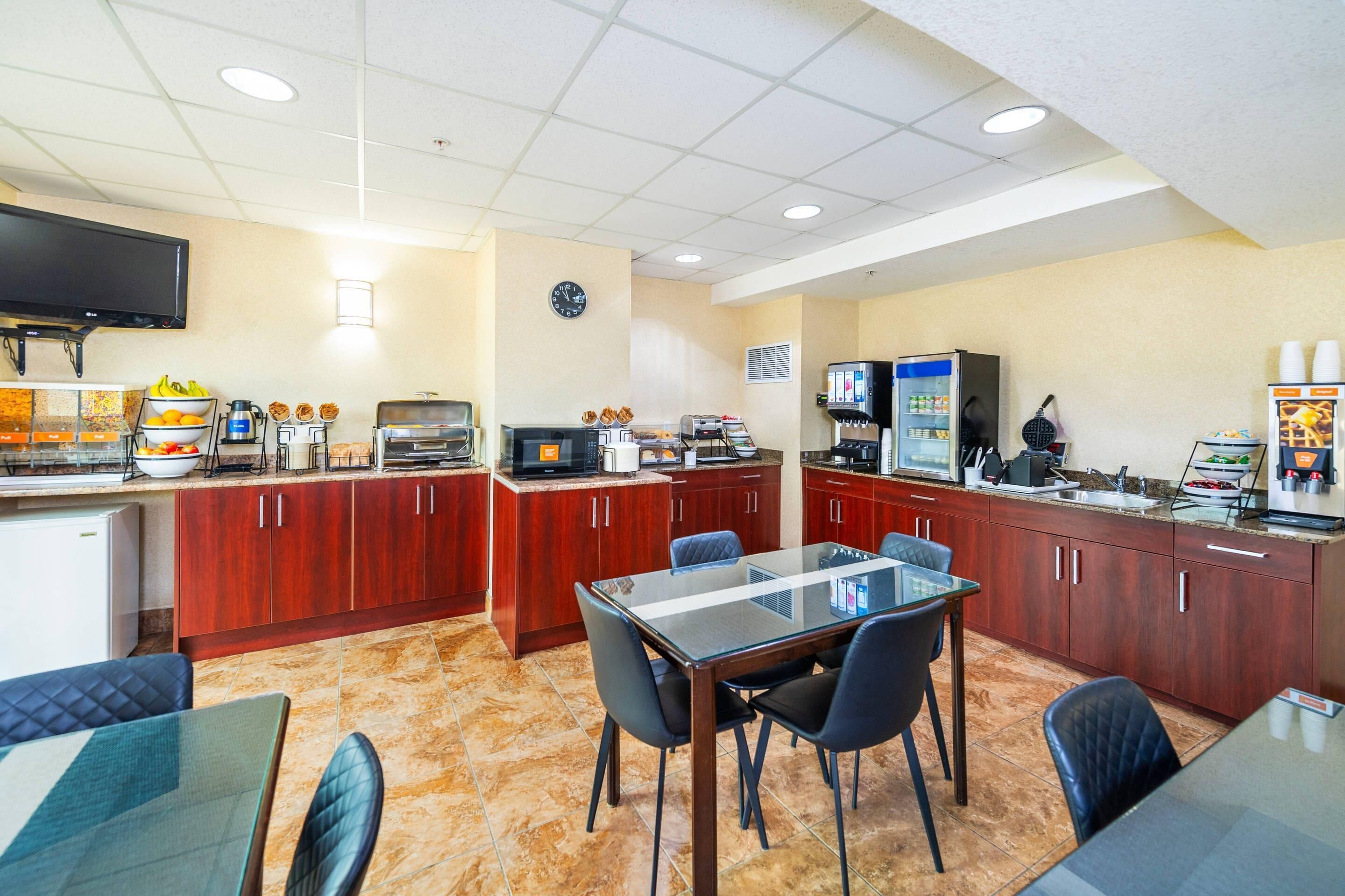 Uma cozinha de hotel com área de refeições, equipada com micro-ondas, máquina de café e grill para waffles.
